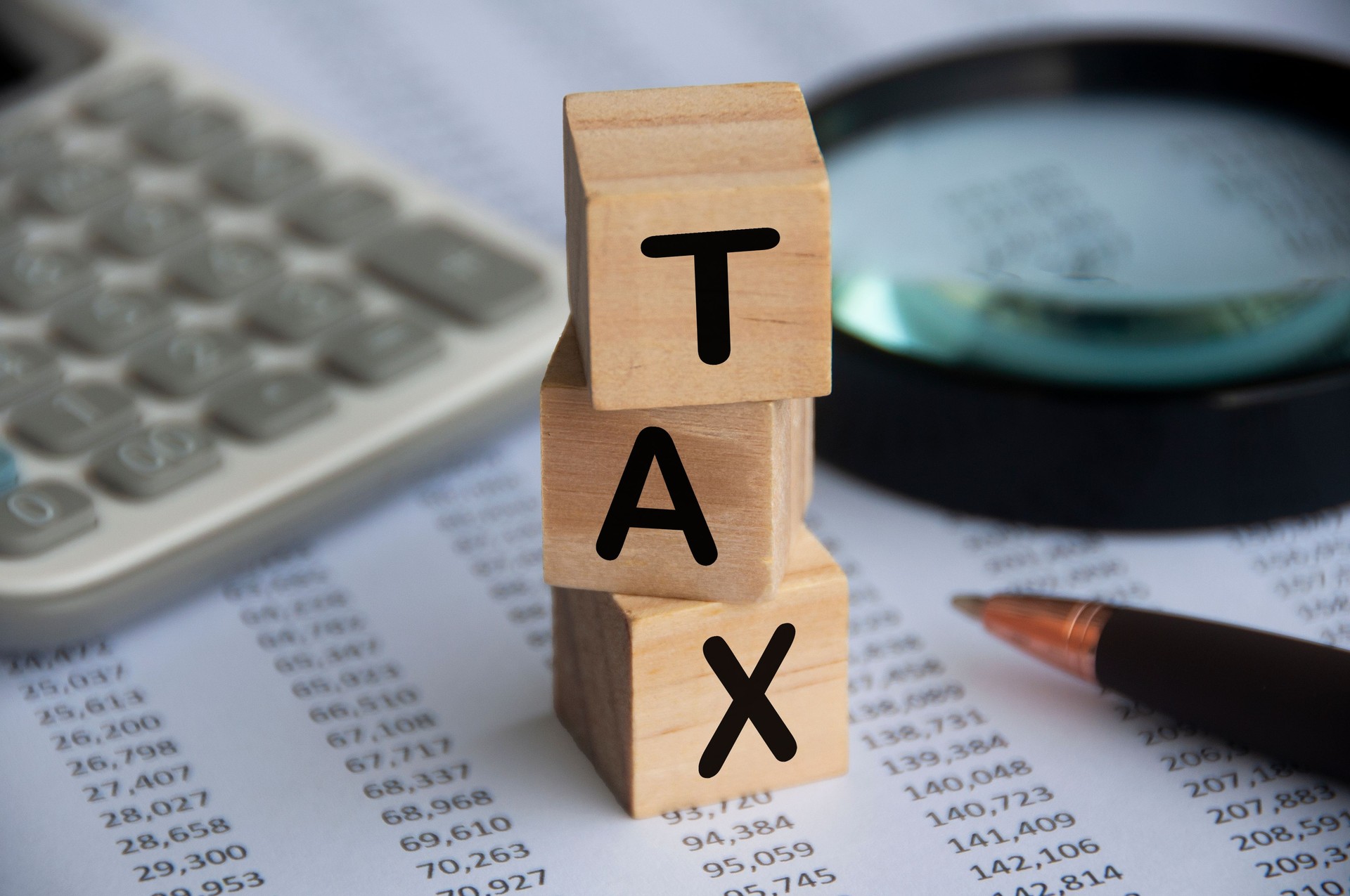 Tax word on wooden blocks with calculator, pen, magnifying glass and data analysis background. Tax concept